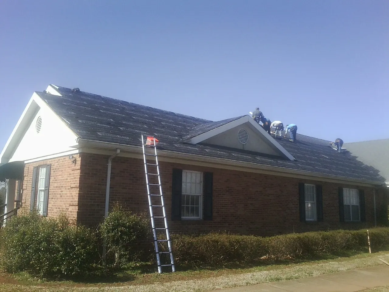 Crew tearing shingles off a brick ranch roof with a ladder set — Metal Roof Repair work by our crew in Bethlehem